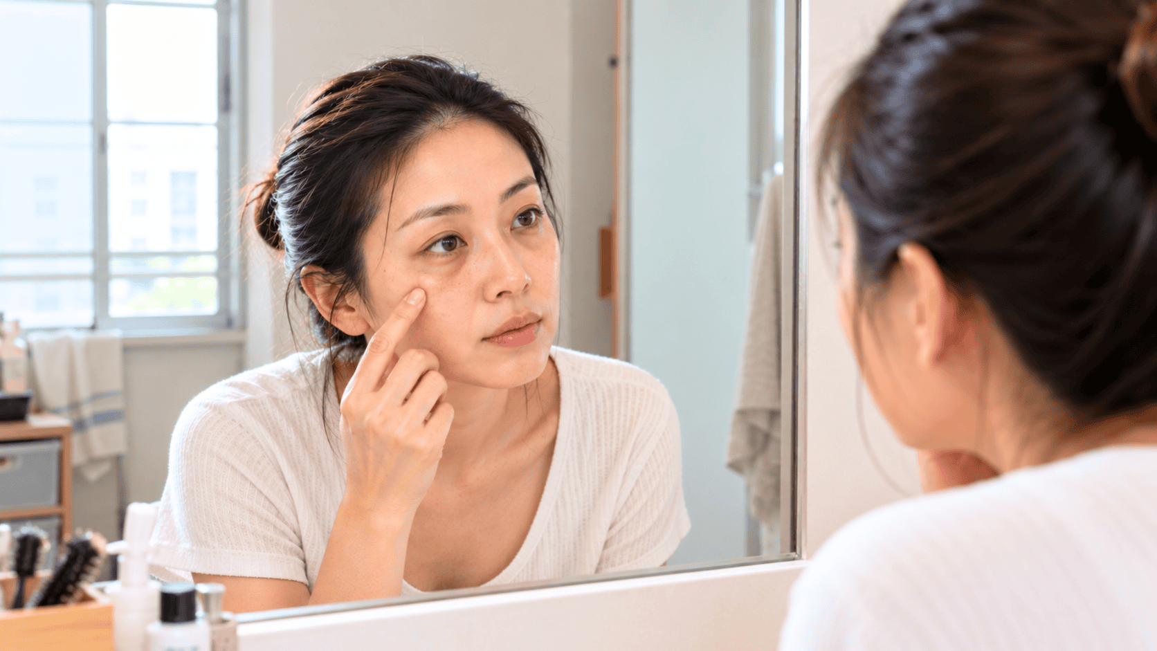 Woman checking the dark circles under her eyes in a bathroom mirror in natural light