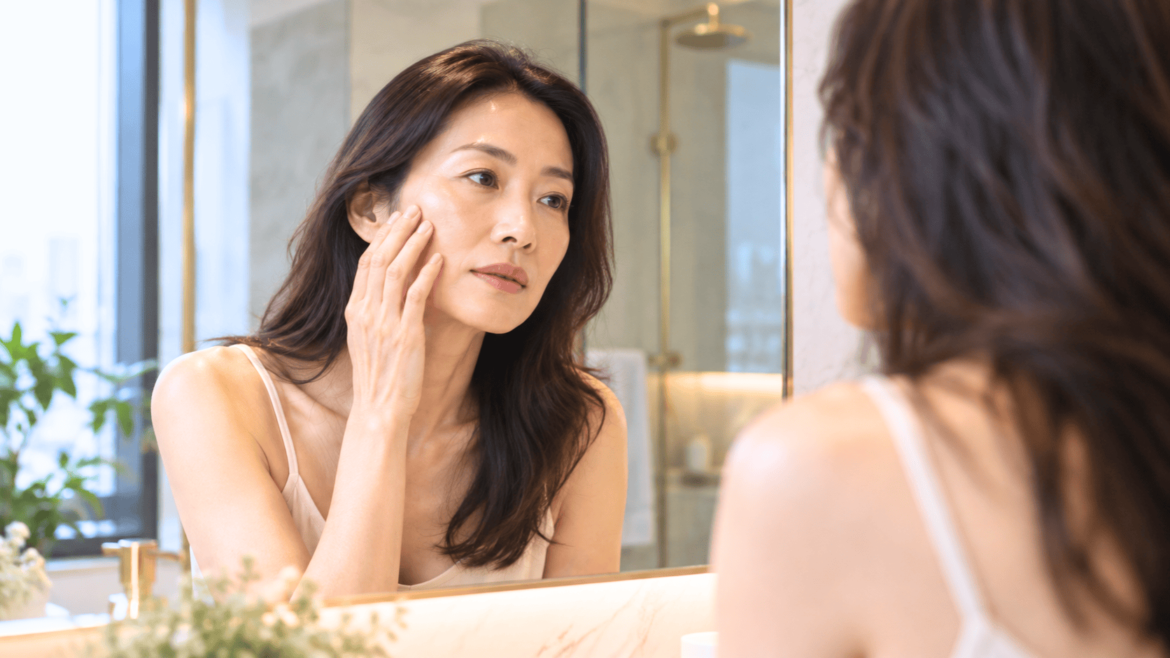 Woman examining flatter cheeks and temple hollowing in a mirror after GLP-1 weight loss